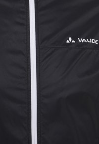 Veste coupe-vent noire avec une fermeture éclair blanche et le logo "Vaude", fabriquée en tissu léger et lisse à texture mate.