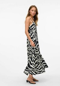 Robe maxi avec un imprimé zèbre noir et blanc. Fabriquée en tissu léger avec un design fluide et des bretelles fines. Sandales noires présentées.