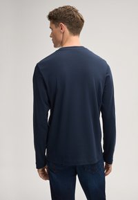 Marineblaue Langarmbluse aus glattem Baumwollstoff; mit Rundhalsausschnitt und entspannter Passform, kombiniert mit dunklen Jeans.