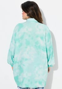 Una camicia a maniche lunghe, ampia, di un verde menta con un motivo tie-dye, caratterizzata da dettagli arricciati alle maniche e un colletto.