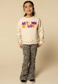 Lichtbeige sweatshirt met veelkleurige tekst "AUTUMN OF LOVE", gecombineerd met zwart-beige panterprint flare pants en zwarte sneakers.
