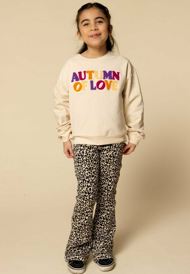 Lichtbeige sweatshirt met veelkleurige tekst "AUTUMN OF LOVE", gecombineerd met zwart-beige panterprint flare pants en zwarte sneakers.