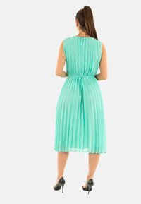 Vestido plisado sin mangas en verde menta con cintura ajustada, falda fluida y largo hasta la mitad de la pantorrilla, combinado con tacones altos negros.