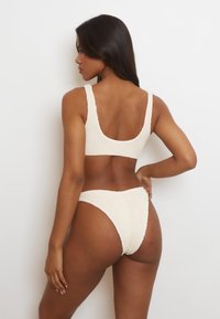 Set bikini color crema con bralette a compressione testurizzato e spalline larghe, insieme a slip alti, entrambi con un design senza cuciture.