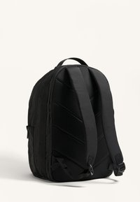 Fekete hátizsák, texturált, párnázott hátrésszel és széles hevederekkel. Az oldalon zigzag mintázat található, valamint egy oldalsó cipzáras zseb a tároláshoz.