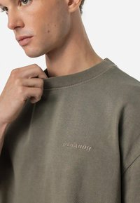 Khaki crewneck sweatshirt with a soft texture, featuring an embossed "PEGAJOR" logo on the chest and ribbed collar detail.