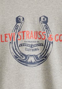 Sudadera gris con un gráfico de herradura azul que dice "Levi Strauss & Co." en texto rojo y las palabras "Ropa remachada de cobre."