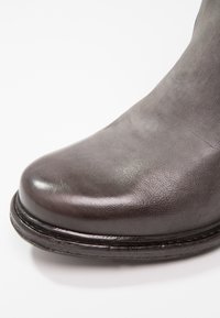 Dunkelgrauer Lederstiefel mit runder Zehenform, glatter Oberfläche und einer kontrastierenden genähten Sohle. Keine sichtbaren Beschläge oder dekorativen Akzente.