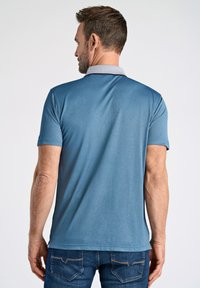 Blå polo-shirt med kontrasterande krage, korta ärmar och slät textur; bärs med mörka denimjeans, visande bakvy.