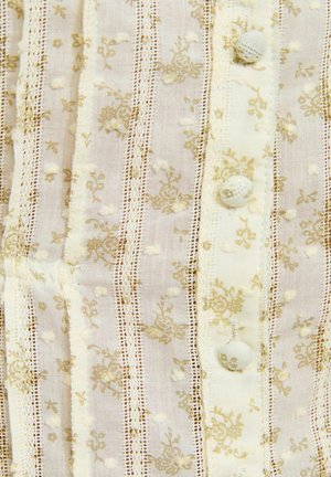 Tissu crème avec des rayures de dentelle verticales, des points texturés, de petits motifs floraux et trois boutons recouverts de tissu en gros plan.