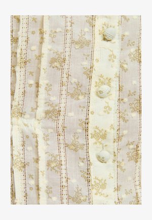 Tissu crème avec des rayures de dentelle verticales, des points texturés, de petits motifs floraux et trois boutons recouverts de tissu en gros plan.