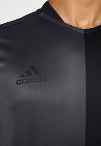 Černé sportovní tričko s texturovaným povrchem, s protilehlým leskem na jedné straně a s embosovaným logem Adidas na hrudi.