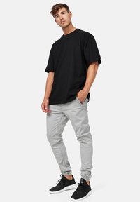 Camiseta negra de gran tamaño, pantalones gris ajustados y zapatillas negras. La camiseta tiene un escote redondo; los pantalones cuentan con puños elásticos.
