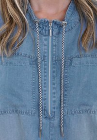 Hellblaue Denim-Halbzip-Jacke mit zwei Brusttaschen, einstellbarem Kordelzug-Kapuze und kontrastierenden geflochtenen Kordeln.
