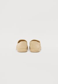 Scarpe slip-on beige con finitura testurizzata, tomaia in tessuto morbido e suola in corda di juta; presenta un logo sul retro e un design minimalista.