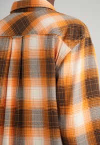 Camicia in flanella con un motivo a quadri arancione, grigio e marrone, colletto a bottoni e dettaglio del giromanica sul retro. Tessuto testurizzato.