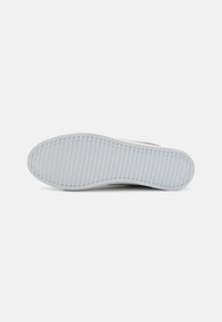 White rubber shoe sole with textured surface, featuring horizontal ridges and grooves for traction. Rounded toe and smooth edges.