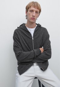Mörkgrå zip-up hoodie med huva och ribbade muddar, bärs över en vit t-shirt. Enkelt mönster, mjuk textur och minimalistisk stil.