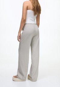 Pantalons larges gris clair avec une texture douce, associés à un top blanc sans bretelles avec un ourlet à volants. Le mannequin porte des sandales à plateforme.