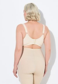 Beige bh met verstelbare banden, haak- en oogsluiting en een gladde textuur, gecombineerd met een bijpassend beige hoge taille kledingstuk.