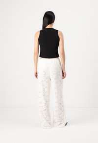 Top scurt fără mâneci, de culoare neagră, asortat cu pantaloni largi din dantelă albă, având modele florale și accente texturate.