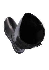 Bottines en cuir noir avec un panneau élastique texturé, bout rond et semelle en caoutchouc plate. L'intérieur est lisse avec une languette à l'arrière.