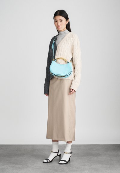 Light blue suede handbag with gold accents, worn with a beige midi skirt and a textured gray and cream sweater. Black strappy heels and white socks.