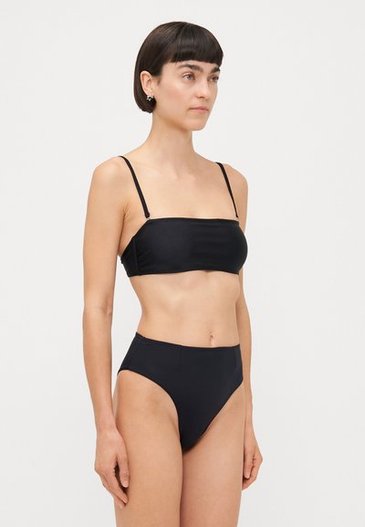 Schwarzes Bikini-Set mit einem Bandeau-Oberteil und dünnen Trägern sowie hochgeschnittenen Unterteilen. Glatte Textur, minimalistisches Design und keine zusätzlichen Muster.