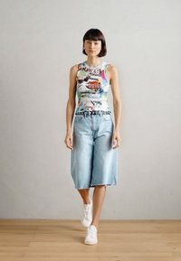 Αμάνικη, πολύχρωμη μπλούζα με σχέδιο συνδυασμένη με ανοιχτό μπλε, φαρδιά κοντά τζιν. Άσπρα αθλητικά παπούτσια ολοκληρώνουν την εμφάνιση.