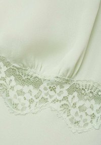 Light green fabric with a smooth texture, featuring a delicate lace trim along the bottom, showcasing floral patterns and scalloped edges.