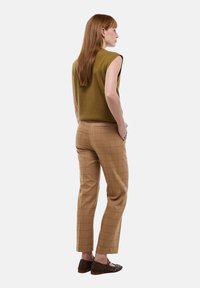 Haut sans manches vert olive associé à un pantalon à carreaux marron et des ballerines tressées marron, vu de dos, mettant en valeur l'ajustement de la tenue.