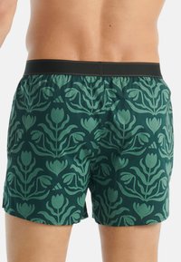Boxershorts med ett grönt blommönster på en mörk bakgrund, med en elastisk svart midja och en slät tygkvalitet.