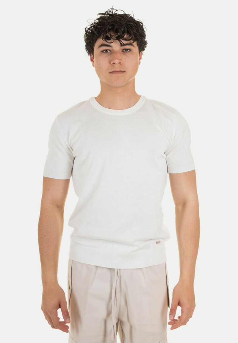 Maglione bianco in cotone a maniche corte con colletto a girocollo. Design aderente con polsini e fondo a costine. Tessuto liscio con un piccolo logo sulla vita.