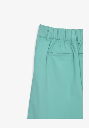 Helle Türkishosen mit elastischem Bund, Falten und einer Gesäßtasche. Hergestellt aus glattem Stoff und mit minimalen Nähdetails versehen.