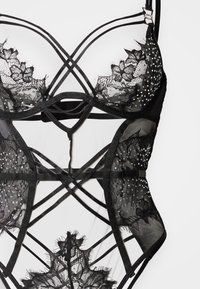 Μαύρο κορμάκι από δαντέλα με διάφανα τμήματα, περίπλοκα λουλουδένια σχέδια και λουριά που διασταυρώνονται, με κρυστάλλινα διακοσμητικά σε όλο το σχέδιο.