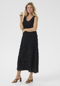 Black crochet maxi dress with a scoop neckline and intricate circular patterns. Paired with brown block-heel sandals.