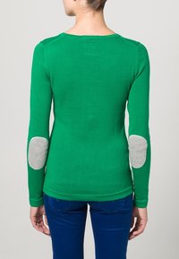 Zelený svetr s dlouhým rukávem, výstřihem do oblouku a šedými náplastmi na loktech. Látka působí hladce, svetr má přiléhavý střih a žebrovaný lem.