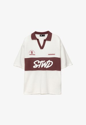 Bijela kratka majica s ovratnikom boje burgundca i horizontalnom trakom boje burgundca. Sadrži izvezene natpise i zvjezdice u crvenoj i bijeloj boji.