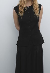 Black sleeveless top with a fitted bodice and button front, transitioning to a flared hem; paired with a matching black, pleated skirt.