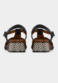 Μαύρα δερμάτινα σανδάλια με υφή, που διαθέτουν τακούνι με γεωμετρικό σχέδιο σε μαύρο και κρεμ. Ρυθμιζόμενο λουράκι αστραγάλου για ασφαλή εφαρμογή.