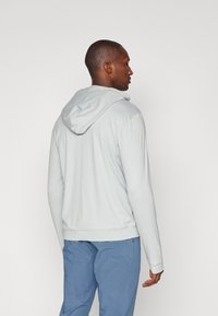 Sweatshirt cinza claro com capuz, com uma textura suave e punhos ajustados, combinado com calças azuis xadrez. Design minimalista, sem padrões proeminentes.