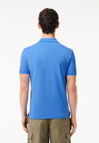 Blå polo skjorta tillverkad av andningsbart material, med krag nacke och korta ärmar. Slät textur med en enfärgad design.