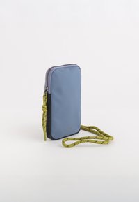 Modrá nylonová kabelka přes rameno s kontrastním černým dnem, zapínáním na zip a žlutým vzorovaným popruhem. Obsahuje logo na přední straně.