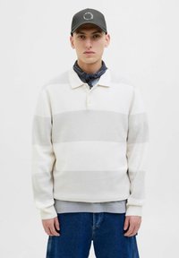White striped pullover with gray horizontal bands, featuring a collar, three buttons, and ribbed cuffs, worn over a gray shirt and blue jeans.
