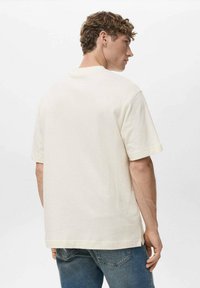 T-shirt in cotone crema con maniche corte, vestibilità comoda e scollo rotondo. La texture appare morbida, con un design semplice e discreto.