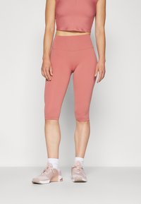 Różowy, dopasowany crop top w połączeniu z pasującymi legginsami do kolan, oba wykonane z gładkiego, elastycznego materiału. Noszony z lekkimi, różowymi trampkami.