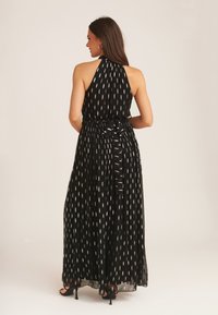 Black maxi dress with a halter neck, pleated skirt, and a tied waist, featuring an irregular white pattern throughout the fabric.