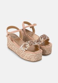 Sandales compensées roses avec une semelle en paille tissée, présentant une sangle ornée de bijoux à l'avant et un détail de boucle sur la sangle de la cheville.