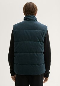 Navy Steppweste mit hohem Kragen und gesteppter Optik, aus strukturiertem Material und in lässiger Passform, getragen über einem schwarzen Strickpullover.