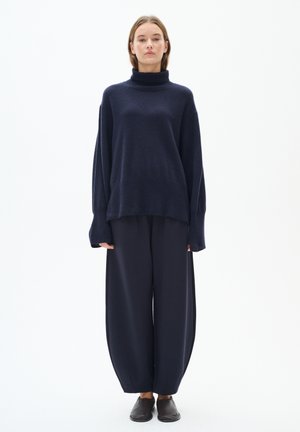 Marinblå polotröja med vida ärmar, tillsammans med löst sittande marinblå byxor. Släta ytor, minimalistisk design och diskret stil.